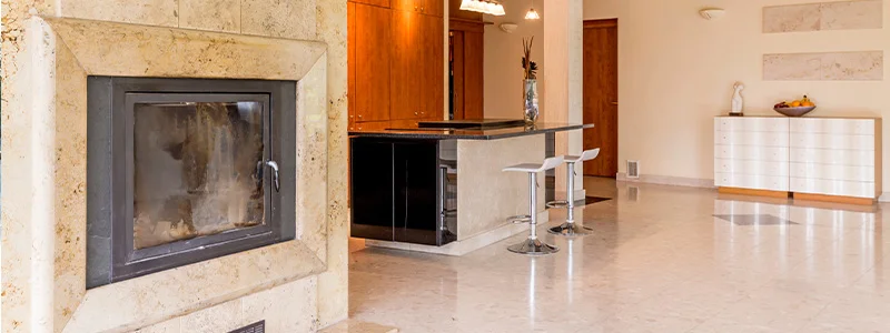 Modern open-concept living area with a stone-framed fireplace on the left, and a kitchen island with two white bar stools in the center rail.