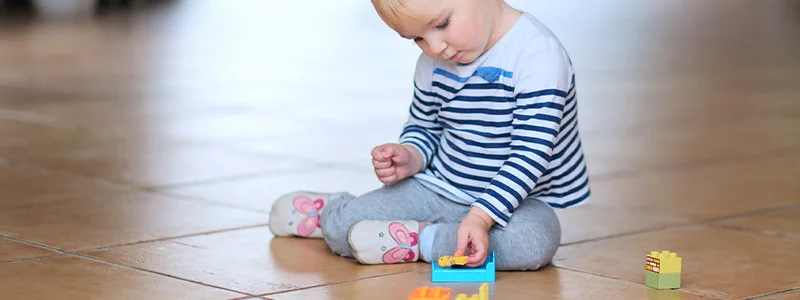 Toddler sitting on a tiled floor, playing with colorful building blocks and a small toy car nearby.
